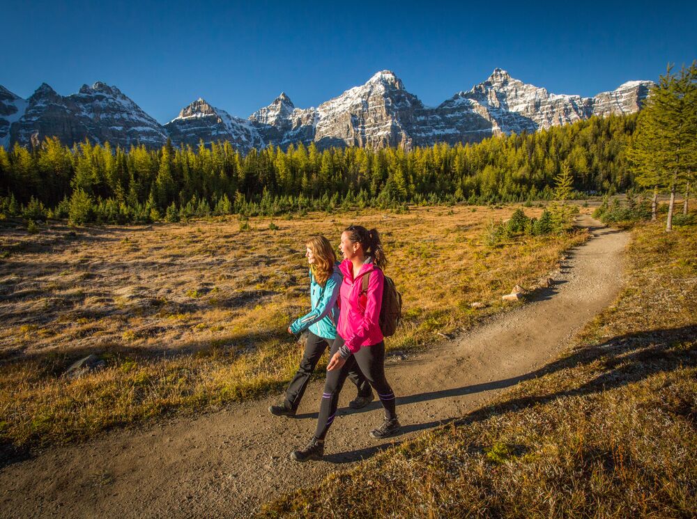 Two women walk in Larch Valley with mountain peaks behind them in Banff National Park. 